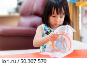Asian girl child sewing in living room at home as home schooling while city lockdown because of covid-19 pandemic across the world. Home Schooling prepare for Preschool concept. Стоковое фото, агентство Ingram Publishing / Фотобанк Лори