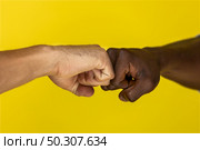 foreground european and afroamerican hand to hand clenched into fists on the yellow background. Стоковое фото, агентство Ingram Publishing / Фотобанк Лори