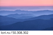 Mountain ridges in fog at sunset in autumn. Beautiful landscape with foggy mountain valley, rocks, forest, pink sky in fall at dusk in blue hour. Aerial view of hills. Top view. Nature background. Стоковое фото, агентство Ingram Publishing / Фотобанк Лори