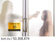Silhouette of medical staff with PPE suit taking temperature to asian woman before do coronavirus test with signage of COVID-19 quarantine zone. New normal healthcare service and medical concept. Стоковое фото, агентство Ingram Publishing / Фотобанк Лори