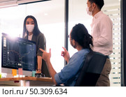 Three asian business person discuss their work in morning after office reopen due to coronavirus COVID-19 pandemic. They wear protective face mask to prevent infection. New normal office life concept. Стоковое фото, агентство Ingram Publishing / Фотобанк Лори