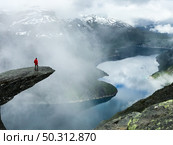 Man sits at the end of Trolltunga before the mountains. Стоковое фото, агентство Ingram Publishing / Фотобанк Лори