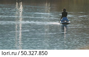 A girl sitting on her knees calmly floats a paddleboard on a sparkling lake. The still water reflects the soft light. Back view. Riding on sup board. Стоковое видео, видеограф Воловодов Владимир / Фотобанк Лори