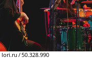 Close-up of a musician playing a bass guitar, his hands deftly plucking strings. In background partially visible is a drummer behind a drum kit and a girl behind conga drums. A jazz band is on stage. Стоковое видео, видеограф Воловодов Владимир / Фотобанк Лори