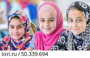 A group of young girls, wearing vibrant hijabs, shares a joyous moment together, possibly during a school event. Стоковое AI-изображение, AI-художник Данила Большаков / Фотобанк Лори