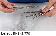 Two hands holding a selection of metal drill bits on a smooth marble surface. Стоковое фото, фотограф Анастасия / Фотобанк Лори