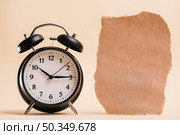 blank brown torn paper near black alarm clock against colored backdrop. Стоковое фото, агентство Ingram Publishing / Фотобанк Лори