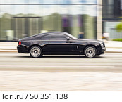 Rolls-Royce Wraith rides on street on high speed. Black premium car with twin-turbocharged V12 engine in fast motion, side view. Редакционное фото, фотограф Константин Григорьев / Фотобанк Лори
