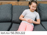 portrait girl sitting gray sofa having sever pain stomach. Стоковое фото, агентство Ingram Publishing / Фотобанк Лори