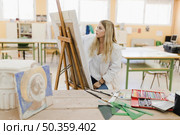 blonde young woman sitting workshop painting easel. Стоковое фото, агентство Ingram Publishing / Фотобанк Лори