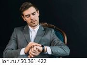 young man checking time his watch against black background. Стоковое фото, агентство Ingram Publishing / Фотобанк Лори
