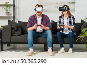 young couple sitting sofa using virtual reality glasses playing video game with joystick. Стоковое фото, агентство Ingram Publishing / Фотобанк Лори