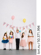 birthday boy standing with girls against white wall decorated with bunting. Стоковое фото, агентство Ingram Publishing / Фотобанк Лори