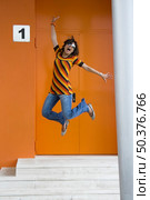 Cosmopolitan girl jumping of happiness in front of a orange building. Стоковое фото, агентство Ingram Publishing / Фотобанк Лори