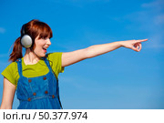 Portrait of a happy woman listen music over a beautiful blue sky and pointing to somewhere. Стоковое фото, агентство Ingram Publishing / Фотобанк Лори