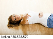 Beautiful young woman lying on floor and pointing to you. Стоковое фото, агентство Ingram Publishing / Фотобанк Лори