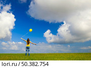 Happy young woman with a yellow balloon on a green meadow. Стоковое фото, агентство Ingram Publishing / Фотобанк Лори
