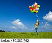Happy young woman with colorful balloons on a green meadow. Стоковое фото, агентство Ingram Publishing / Фотобанк Лори
