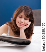 Beautiful young girl lying on the bed and reading the newspaper. Стоковое фото, агентство Ingram Publishing / Фотобанк Лори