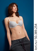 Beautiful young woman wearing a casual lingerie and pajama pants, against a blue wall. Стоковое фото, агентство Ingram Publishing / Фотобанк Лори