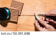 close up man fixing hook with plier near reel cork board wooden desk. Стоковое фото, агентство Ingram Publishing / Фотобанк Лори