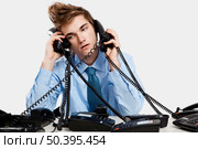 Young man sitting in the office and answering several phones at the same time. Стоковое фото, агентство Ingram Publishing / Фотобанк Лори