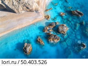 Aerial view of blue sea, rocks in clear water, white sandy beach at sunset in summer. Porto Katsiki, Lefkada island, Greece. Beautiful landscape with sea coast, stones in azure water, waves. Top view. Стоковое фото, агентство Ingram Publishing / Фотобанк Лори