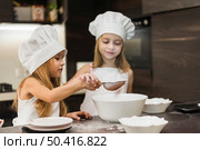 two cute sisters sifting cocoa powder through strainer kitchen. Стоковое фото, агентство Ingram Publishing / Фотобанк Лори