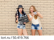 Two beautiful and young girlfriends holding a clapboard, in front of a brick wall. Стоковое фото, агентство Ingram Publishing / Фотобанк Лори