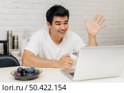 man home during pandemic having video call laptop waving. Стоковое фото, агентство Ingram Publishing / Фотобанк Лори