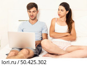 Addicted young man on bed with a laptop while the woman looks angry. Стоковое фото, агентство Ingram Publishing / Фотобанк Лори
