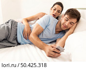 Addicted young man on bed texting  while woman looks angry. Стоковое фото, агентство Ingram Publishing / Фотобанк Лори