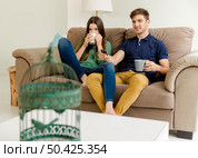 Young couple on the sofa drinking coffee while watching tv. Стоковое фото, агентство Ingram Publishing / Фотобанк Лори