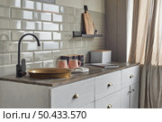 Comfortable small kitchen with old copper sink and modern faucet, gray tiles wall, cabinets, tea and coffee containers, pink cups on wooden counter. Country house kitchen concept.. Comfortable elegant kitchen counter with sink at country house. Стоковое фото, агентство Ingram Publishing / Фотобанк Лори