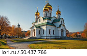 A majestic white Orthodox church with golden domes stands in a park with colorful autumn trees under a blue sky with clouds. Стоковое AI-видео, аниматор Sergey Grishin / Фотобанк Лори