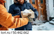 A person in a warm orange jacket hands a package to a recipient on a cold, snowy day. Стоковое AI-изображение, AI-художник Данила Большаков / Фотобанк Лори