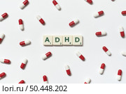 ADHD word formed of scrabble blocks and pharmaceutical pills strewn over white background. Attention deficit hyperactivity disorder and mental health awareness.. ADHD blocks and pharmaceutical pills over white. Стоковое фото, агентство Ingram Publishing / Фотобанк Лори