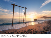 Wooden swing in beautiful blue sea with waves, sandy beach, sky with golden sunlight at sunset in summer. Vacation in Oludeniz, Turkey. Tropical landscape with swing on sea coast, water. Travel. Стоковое фото, агентство Ingram Publishing / Фотобанк Лори