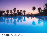 Beautiful reflection in swimming pool at colorful sunset. Purple sky reflected in water, palm trees, sun beds, umbrellas at night in summer. Luxury resort. Landscape with empty pool in twilight. Стоковое фото, агентство Ingram Publishing / Фотобанк Лори