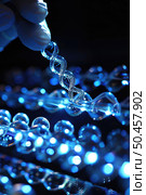 A gloved scientist adjusts a transparent, illuminated model of DNA strands, emphasizing advanced genetic research. Стоковое AI-изображение, AI-художник Данила Большаков / Фотобанк Лори