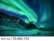 Aurora borealis above frozen beach in Lofoten islands, Norway. Beautiful northern lights. Starry sky with polar lights. Night winter landscape with aurora, sea coast, beach and snowy mountains. Nature. Стоковое фото, агентство Ingram Publishing / Фотобанк Лори