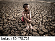 The boy sit hugging their knees bent and looking at the sky to ask for rain on dry soil. Стоковое фото, агентство Ingram Publishing / Фотобанк Лори