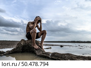 A man sat bent his knees and put his hands on his head, on the base of the tree and surrounded by water. Стоковое фото, агентство Ingram Publishing / Фотобанк Лори