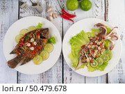 Tilapia fried with chilli sauce and squid, lemon and garlic on a plate on a white wooden table. Стоковое фото, агентство Ingram Publishing / Фотобанк Лори