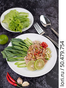 Spicy lime pork salad with kale, galangal, chilli and garlic in a white plate on a black cement floor. Стоковое фото, агентство Ingram Publishing / Фотобанк Лори