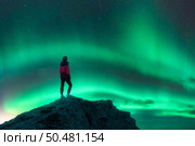 Northern lights and young woman on mountain peak at night. Aurora borealis and silhouette of alone girl on top of rock. Landscape with polar lights. Starry sky with bright aurora. Travel background. Стоковое фото, агентство Ingram Publishing / Фотобанк Лори