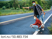 Female tourists sit, male tourists, pretend to hitchhiker Both wearing a mask and on the side of the road. Стоковое фото, агентство Ingram Publishing / Фотобанк Лори