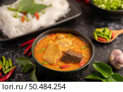 Chicken curry in a black cup with rice noodles, garlic, tomatoes, chilies, and kaffir lime leaves. Стоковое фото, агентство Ingram Publishing / Фотобанк Лори