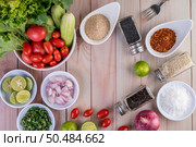Boiled chicken cut into pieces in a white dish, along with lemons, chilies, lemongrass, red onions, chopped onions, tomatoes, sesame, roasted rice, and pepper on a wooden table. Стоковое фото, агентство Ingram Publishing / Фотобанк Лори