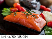 Raw salmon fillets, pepper, kiwi, pineapples, and rosemary onto a plate and black cement floor. Стоковое фото, агентство Ingram Publishing / Фотобанк Лори